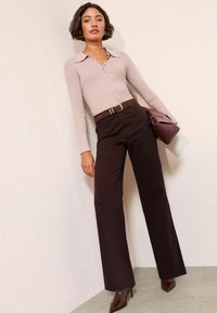 Svijetlo ružičasti rebrasti top s ovratnikom i detaljima na gumbima, uparen s tamnosmešnim hlačama visokog struka i smeškim cipelama na visoku petu. Ljubičasta torbica.