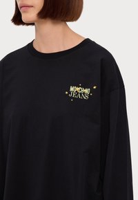 Črna bombažna srajca z dolgimi rokavi, ki se ponaša z rumenim logotipom "Moschino Jeans" in zvezdastimi akcenti na prsih, sproščenega kroja in okroglim izrezom.