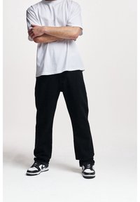 Vit kortärmad t-shirt i kombination med löst sittande svarta byxor. Skorna är svarta och vita sneakers med låg siluett.