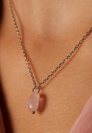 Zilveren ketting met een glad, langwerpig rozenkwarts hanger met een metalen accent aan de onderkant, rustend op de huid.