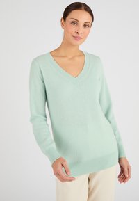Pull V-neck vert menthe en tissu doux, avec des manches longues et un ourlet côtelé. Texture lisse avec peu de détails.