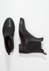 Botas de tobillo de goma negra con un acabado suave, paneles laterales elásticos y un tacón bajo y cuadrado. Presentan una cinta de agarre y detalles de costura sutiles.