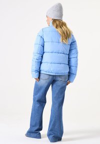 Lichtblauwe pufferjack met een gewatteerd ontwerp, hoge kraag en elastische zoom. Gecombineerd met wijde denim jeans en een grijze gebreide beanie.