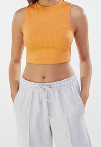Top corto a coste arancione con un collo alto, abbinato a pantaloni della tuta grigi con vita elastica e tasche laterali.