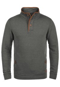 Felpa grigia con collo alto, dettagli in marrone, due bottoni all'esorso e tasche laterali. Tessuto morbido e testurizzato.