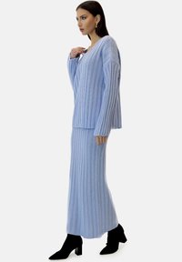 Ensemble composé d'un pull en maille côtelée bleu clair et d'une jupe assortie. Manches longues et coupe allongeante. Associé à des bottines noires à talons.
