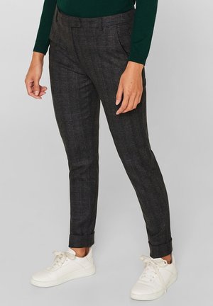 Personne portant un pantalon slim à carreaux gris foncé avec revers, associé à des baskets blanches et un haut à manches longues vert foncé.