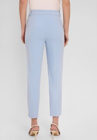 Jasnoniebieskie dopasowane spodnie o gładkiej fakturze i prostym kroju, z bocznymi rozporkami, w połączeniu z beżowymi sandałami na obcasie.
