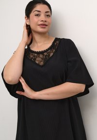 Vestido negro con mangas cortas acampanadas y un panel de encaje alrededor del escote. Tejido texturizado con rayas verticales.