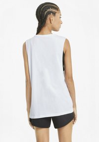 Vit ärmlös jersey-top med en avslappnad passform, mjukt tyg och en något längre bakhem, kombinerad med svarta shorts.