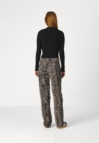 Crni rebrasti top s dugim rukavima uparen s bež hlačama s leopard uzorkom. Hlače imaju opušteni kroj i naglašene su suptilnim sjajem.