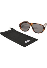 Lunettes de soleil octogonales avec un motif écaille de tortue et des verres gris, accompagnées d'une pochette en tissu noir portant le logo "URBAN CLASSICS".