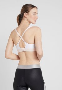 Lys rosa treningsbh med kryssede stropper, justerbar krok-lukking, og mesh-detaljer på ryggen. Kombinert med svarte leggings.