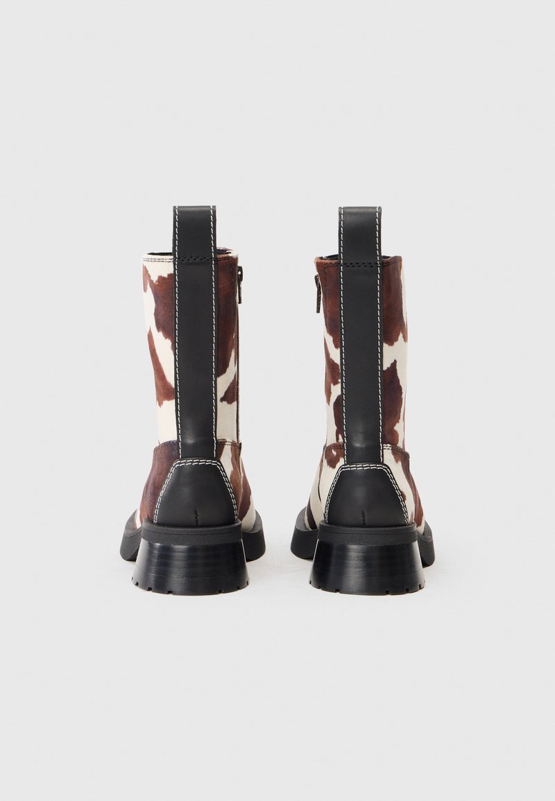 Brown and white cow print ankle boots with black leather accents, a rear zipper, and chunky black heel. Stitched detailing visible.