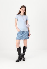 T-shirt azzurro fitted con un piccolo logo rosso, gonna di jeans con branding bianco e stivali neri in vernice fino al ginocchio. Piccola borsa rosa.