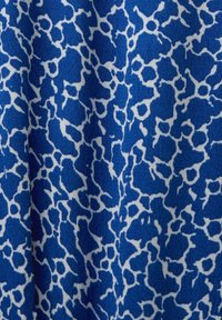 Tissu bleu avec des taches blanches irrégulières dans un style abstrait imprimé animalier, montrant des plis doux et une texture.