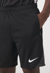 Schwarze Nike Sportshorts aus strukturiertem Material, mit elastischem Bund, Seitentaschen und einem weißen Logo-Akzent am unteren linken Saum.