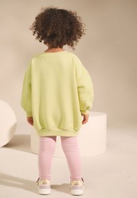 Light green oversized sweater with textured fabric, slouchy sleeves, and ribbed cuffs, paired with pink leggings and white sneakers.