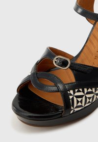 Μαύρο δερμάτινο σανδάλι με γεωμετρικό μοτίβο σε λευκό και μαύρο, ανοιχτό δάκτυλο, λουράκι αστραγάλου και ρυθμιζόμενο μεταλλικό κούμπωμα.