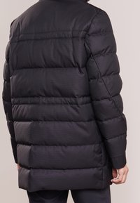 Svart puffjacka med ett kviltat mönster, som har en något längre skärning, hög krage och ribbade manschetter för extra isolering.