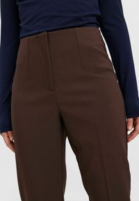 Braune maßgeschneiderte Hosen mit glatter Textur, flachem Bund, seitlichen Taschen und einem sauberen Bügelfalte an der Vorderseite.