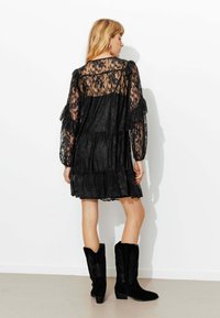 Robe en dentelle noire avec manches à volants et ourlet à volants. Complétée par des bottes en daim noir montantes jusqu'au genou, ornées de broderies détaillées.