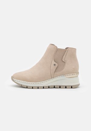 Beige suede ankle boots with a wedge sole, elastic side panels, and contrasting stitching. Textured accents and rounded toe design.