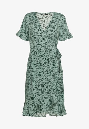 Robe portefeuille vert clair à petits pois noirs, manches courtes volantées, ourlet à volants et lien sur le côté à la taille.