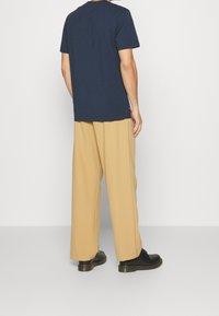 Námořnické bavlněné tričko s krátkým rukávem, v kombinaci s volnými béžovými kalhotami. Černé boty s tlustou podrážkou dotvářejí outfit.