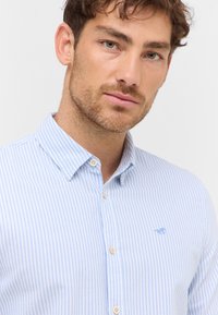 Jasnoniebieska koszula w paski z białymi prążkami, zapinana na guziki, wykonana z bawełny, z klasycznym kołnierzykiem i małym niebieskim logo na piersi.