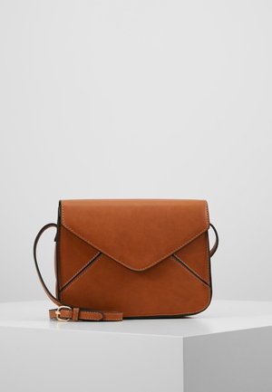 Brązowa skórzana torba na ramię z klapką kopertową i regulowanym paskiem, prezentowana na białym podeście na jednolitym szarym tle.