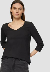 Zwarte 3/4-mouw top, V-hals ontwerp, zachte stof, iets losse pasvorm, gecombineerd met grijze jeans. Minimalistisch, effen kleur, geen zichtbare patronen.