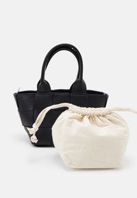 Svart vävt läderhandväska med två handtag bredvid en krämfärgad dragkedjepåse av tyg.