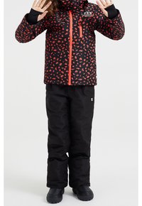 Svart jacka med röd blommönster, framdragkedja och huva. Svarta snöbyxor, svarta stövlar. Händerna lyfta, stående ställning.