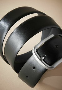 Cinturón de piel negra con una textura suave, que presenta dos bandas paralelas y una hebilla metálica de color plata. Incluye cinco agujeros ajustables.