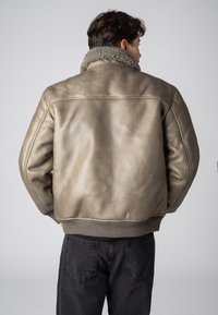 Faux leren bomberjack in olijfgroen met een pluche kraag en geribde manchetten. Beschikt over een gladde textuur en een relaxte pasvorm.