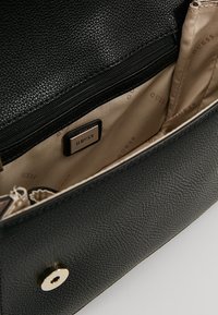 Borsa Guess in pelle nera con texture, aperta per mostrare l'interno in tessuto beige con marchio e una tasca con zip con placca in metallo con logo Guess.