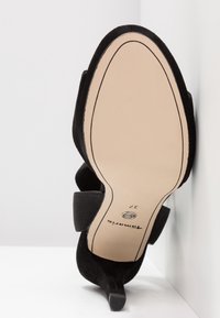 Chaussure noire à talon haut avec semelle beige, détail de bride élastique, taille 37, positionnée droite contre un fond d'angle blanc.