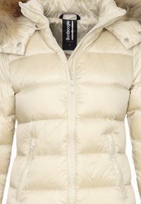 Giacca a vento di colore crema, morbida e imbottita, con cappuccio sfoderabile foderato in pelliccia, chiusura con zip e due tasche laterali con zip. Finitura lucida e texture.