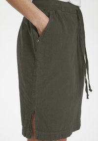 Jupe longueur genou en tissu vert foncé avec une finition texturée, dotée d'une taille ajustable par cordon, de poches latérales et d'une fente à l'ourlet.