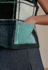 Kootud vest ruudulise mustriga tumesinise, helesinise ja valge värviga. Omab pehmet tekstuuri ja piparmündirohelist tasku.