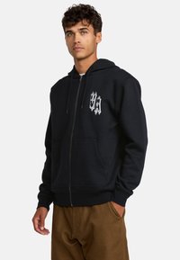 Black zip-up hoodie, made of soft fabric, features a front pocket, adjustable hood, and white graphic logo on the left chest.