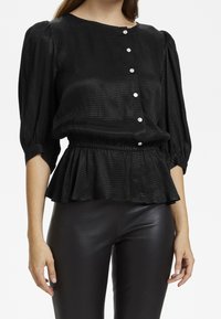 Top peplum negro hecho de tela texturizada, con cuello redondo, mangas abullonadas y acentos de botones plateados en el frente.