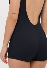 Svart ribbet bodysuit med racerback-design og dyp utskåring bak. Har jevne kanter og en tettsittende passform, med en liten merkeetikett bak.