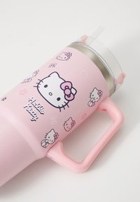 Roza izolirana skodelica z osebami Hello Kitty, s pokrovom za slamico in ročajem. Gladka mat površina z belimi in temno roza akcenti.