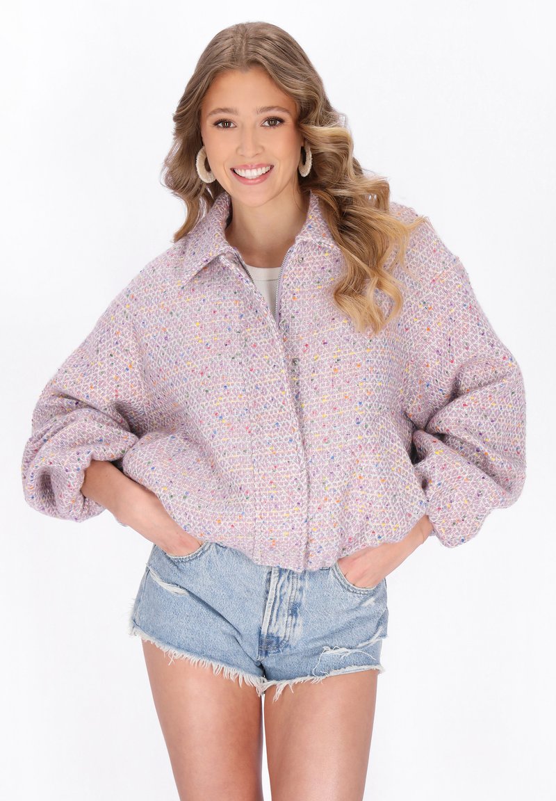 Jasnofioletowa krótka kurtka z fakturowanej tkaniny z wielobarwnymi kropkami, duży kołnierz i oversize'owe rękawy. Nosi się ją na szorty dżinsowe.