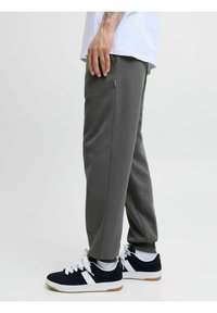Grå joggingbukser lavet af blødt stof, med en tapered design og sidelommer. Kombineret med sorte sneakers og hvide snørebånd, der skaber et afslappet look.
