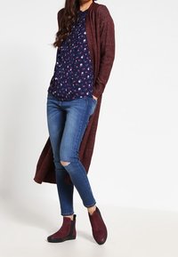 Vínová dlouhá cardigan, námořnická květinová blůza, modré skinny džíny s roztrženými koleny a burgundské kotníkové boty s černou podrážkou.