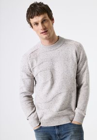 Pull gris clair avec un motif texturé et un col rond côtelé. Présente des accents foncés mouchetés ainsi que des poignets et un ourlet côtelés.
