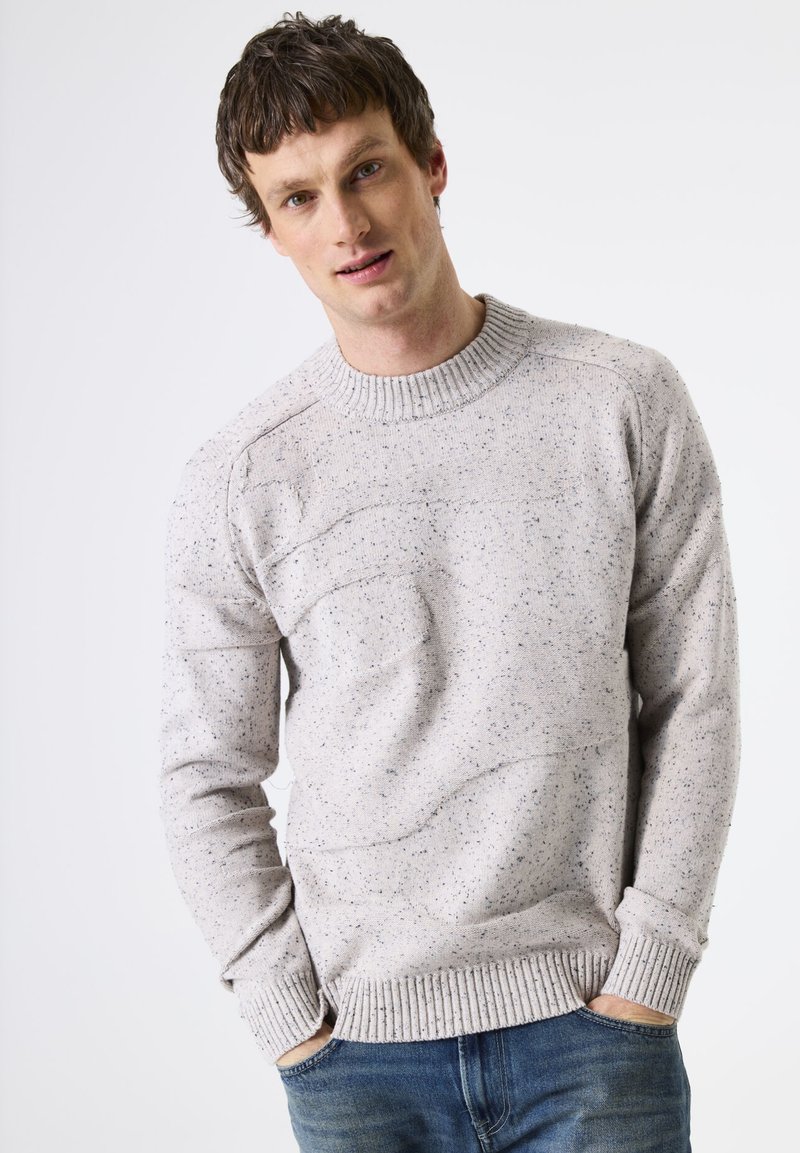 Pull gris clair avec un motif texturé et un col rond côtelé. Présente des accents foncés mouchetés ainsi que des poignets et un ourlet côtelés.